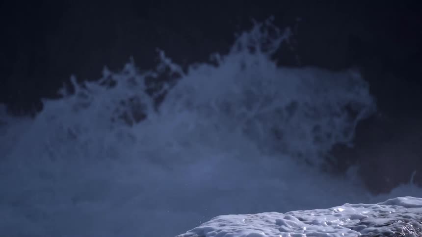 An ocean wave splashes over a rock