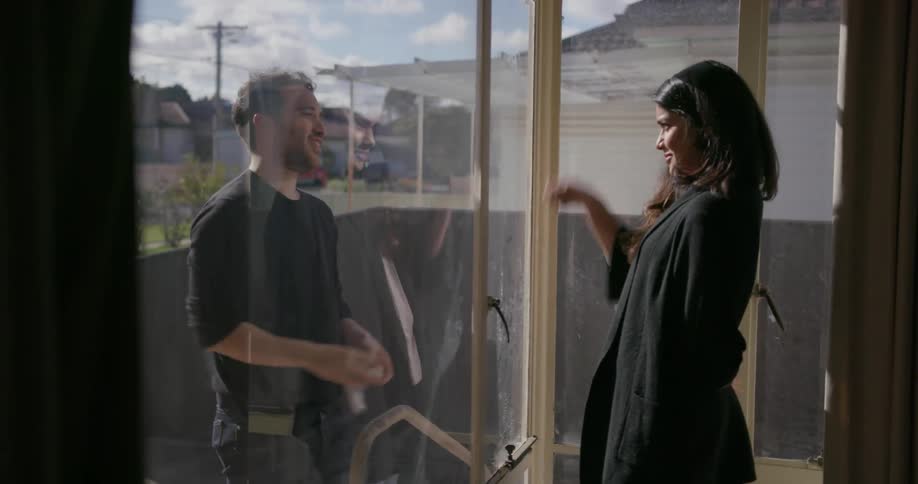 A woman is supervising a man as he cleans the windows on their home