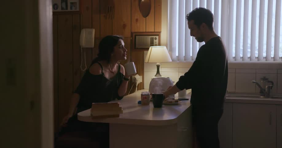 A man and woman drink coffee at a kitchen counter