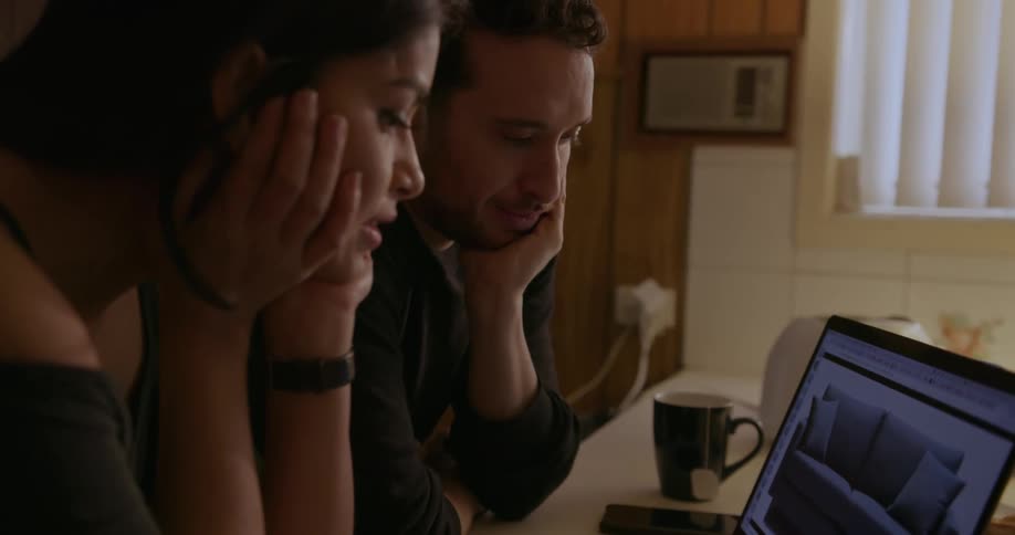 A man and woman are looking at couches on a laptop
