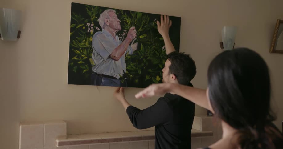 A man hangs a picture while a woman helps