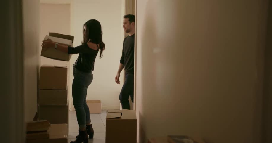 Man and woman carry boxes in a hallway lined with boxes