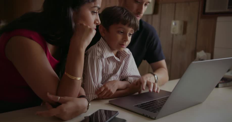 A couple and their son are looking at a laptop and talking inside during the day