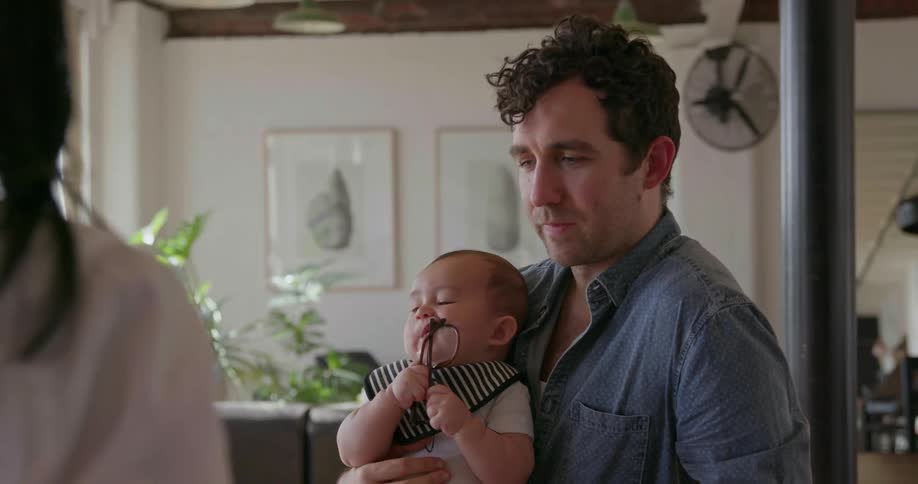 A man holds a baby and talks to a woman at the kitchen counter