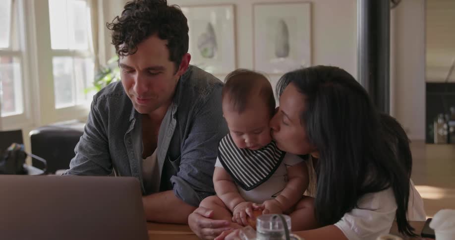 Man woman and baby sit at a table looking at a laptop