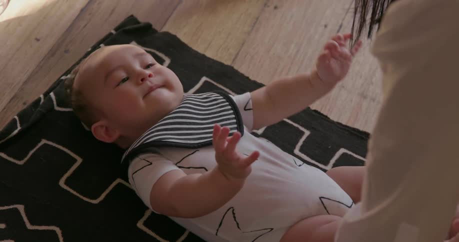A woman stands over her young baby laying on a blanket
