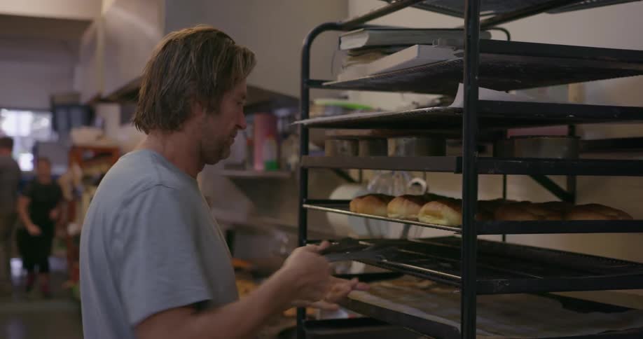 A man puts some pastries on a shelf then removes one