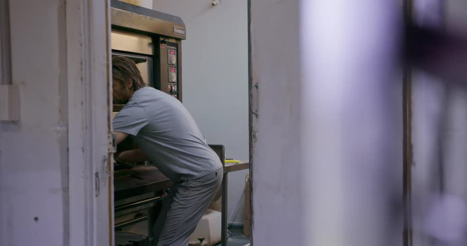 A man removes a tray of rolls from an industrial oven
