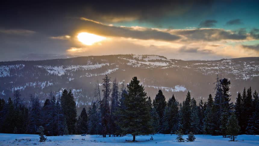 Clouds and snow move in time lapse over a mountain and trees