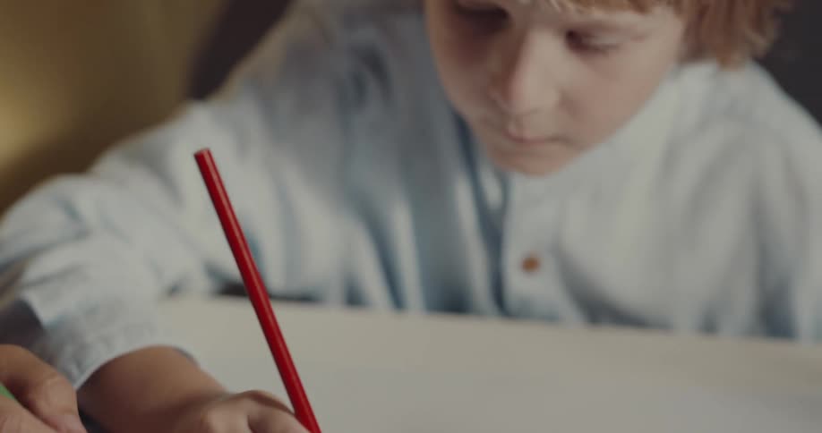 A boy draws with colored pencil with a family member