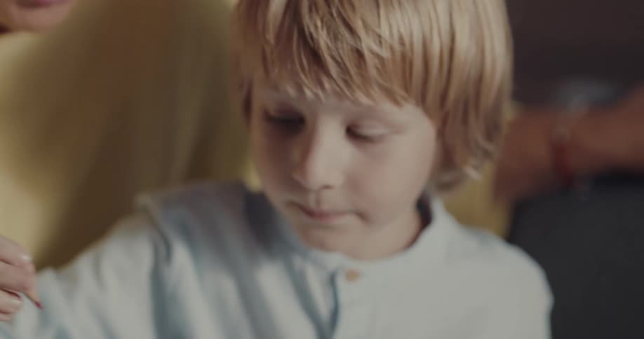 A woman guides a boy as he draws using a colored pencil