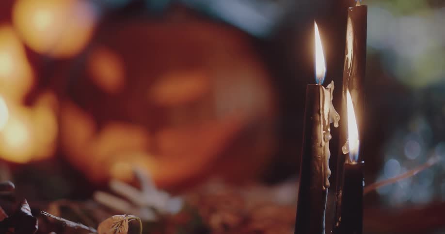 Burning black candles sit on ground near lit jack o lantern at night