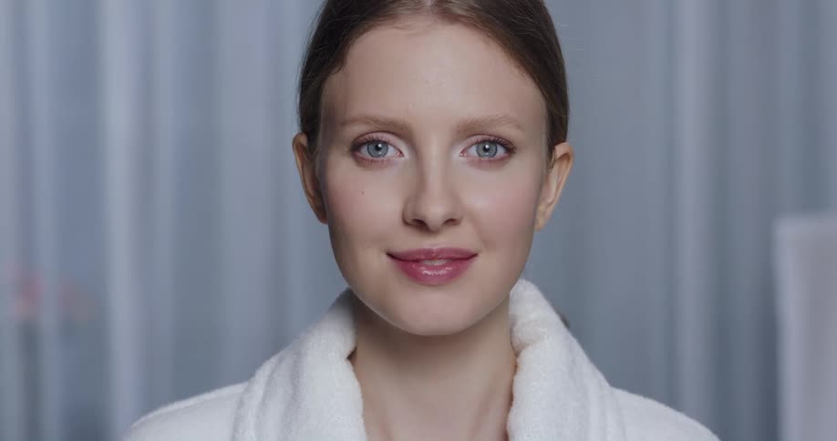 Beautiful female model with makeup and white bathrobe looks at camera smiling