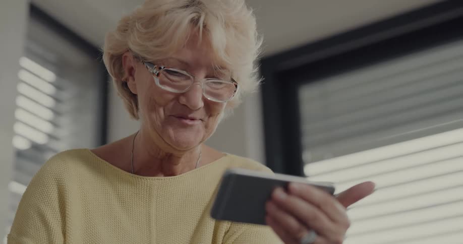 An elderly woman uses a smartphone to participate in a video chat