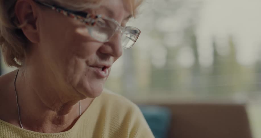 An elderly woman with blond hair and glasses is speaking to someone