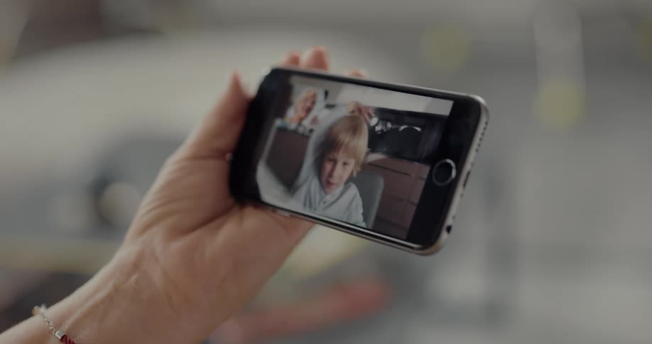 An elderly woman using a smartphone to video chat with a child waves goodbye as the child waves back