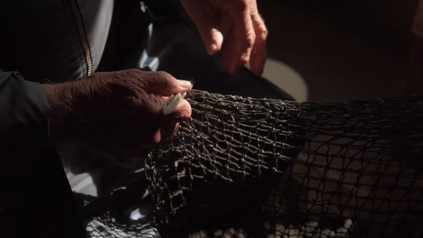 An elderly man sews a fishing net