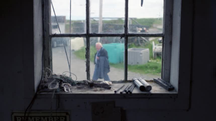 A man is walking outside a window holding his jacket