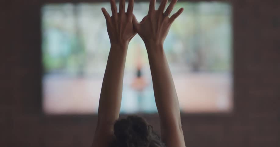 A woman sits in front of a television and stretches along with an exercise video