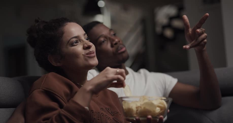Young happy couple talking and laughing while watching movies at home