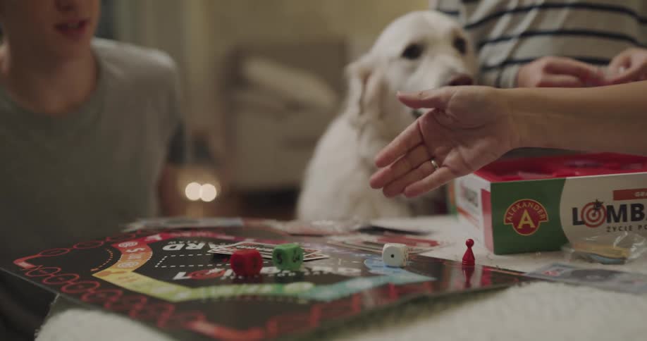 A teenage boy sits next to his dog at home and plays a game with his family