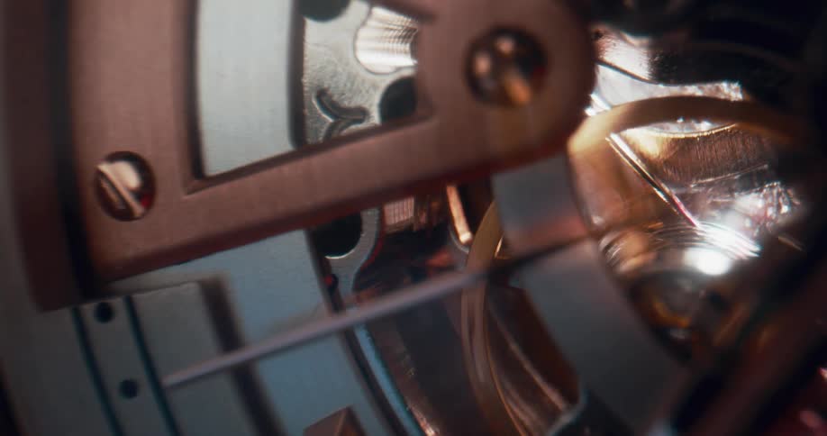 The second hand on a clock ticks by as light shines on the cogs and wheels inside