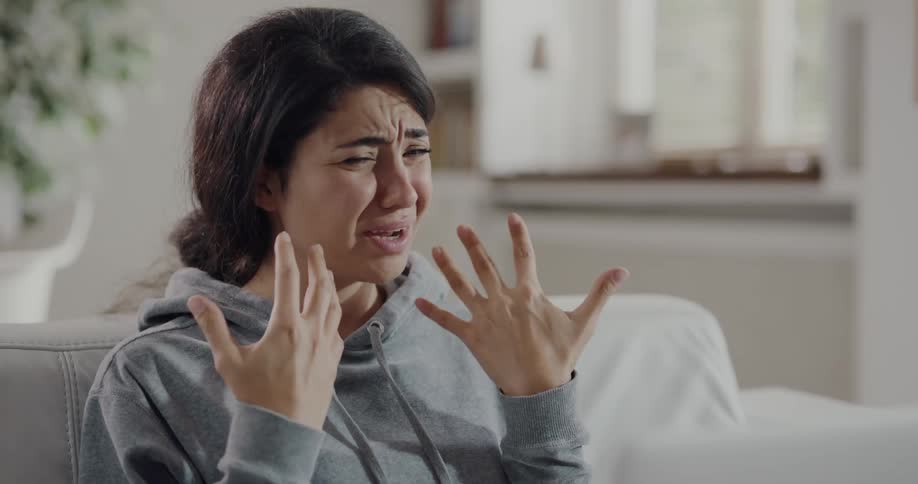 A young woman sits at home and talks and motions about her sore throat