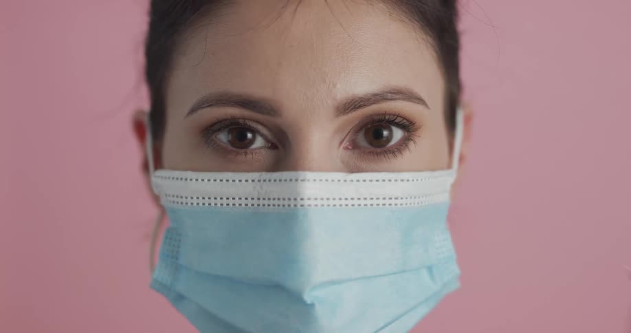 Woman with brown eyes and blue mask faces the camera with eye contact