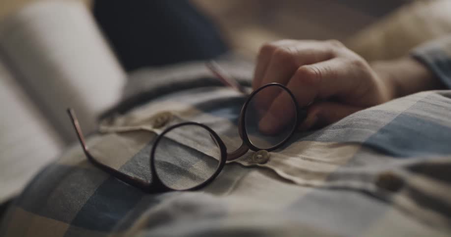 A man is reading a book and holding his glasses