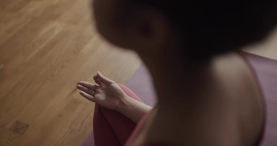 A woman meditates while sitting on a yoga mat indoors