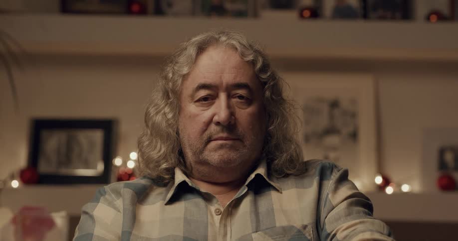 An elderly man sits at home and lifts his eyes up and looks ahead