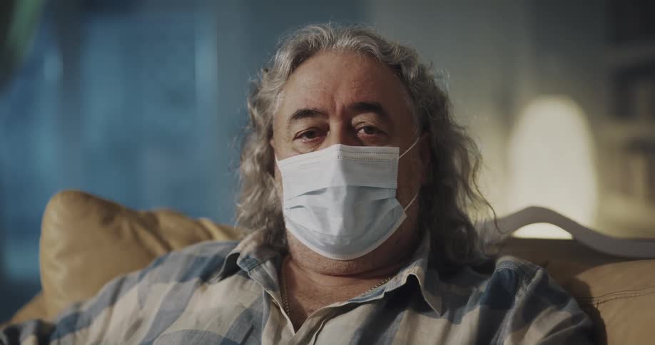 Older man wearing a face mask sitting on couch looking at the camera