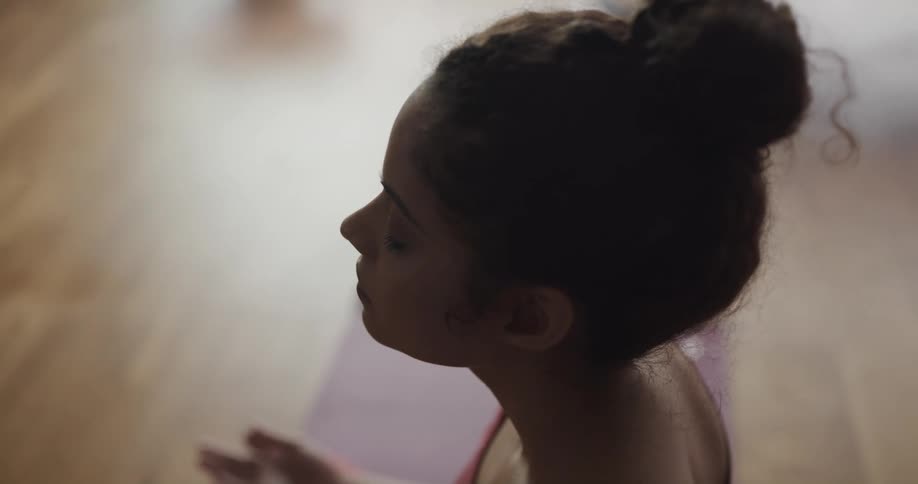 A young woman meditates while sitting on a yoga mat indoors during the day