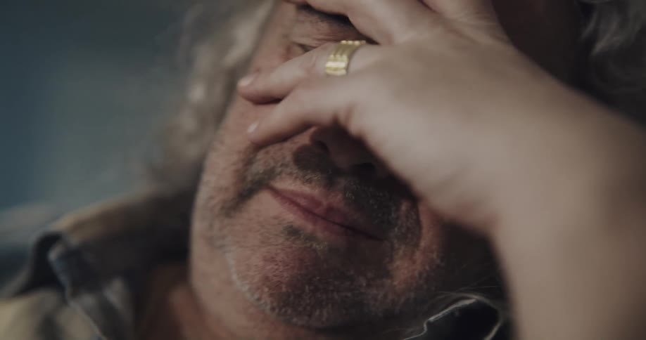 An elderly man puts his head in his hand as he sobs