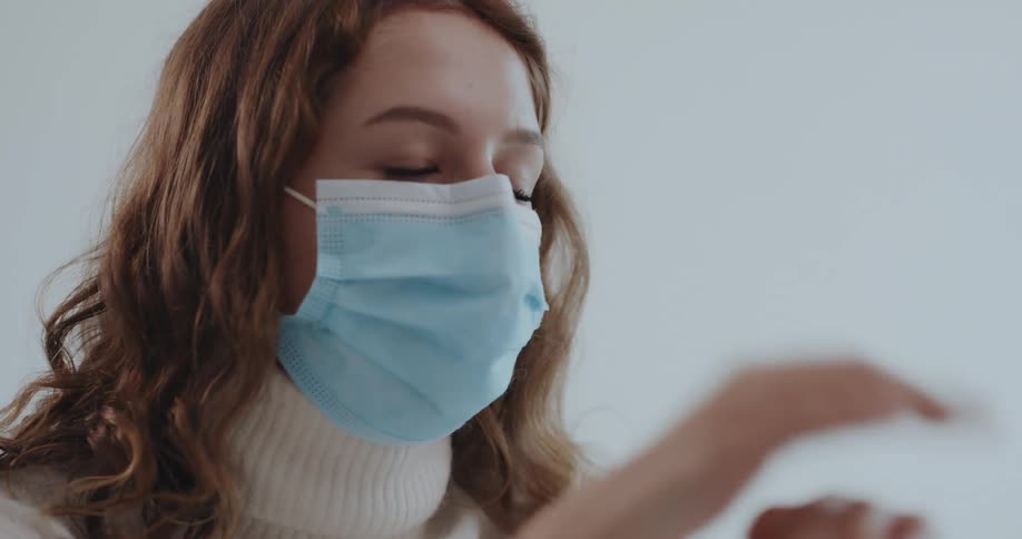 Woman wearing a blue disposable face mask rubs hand sanitizer