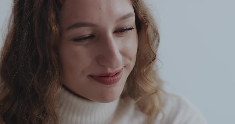 Woman with brown wavy hair and white turtleneck sweater smiles at person