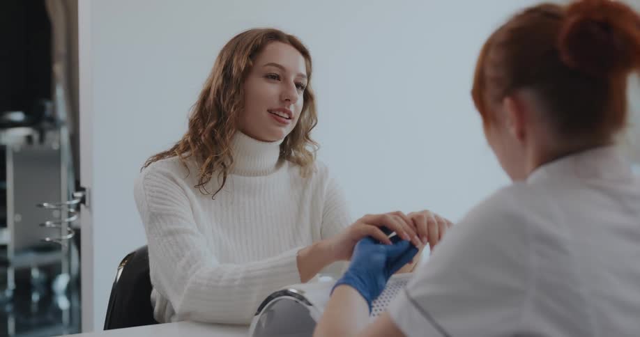 Redheaded manicurist wears gloves while handling clients hands