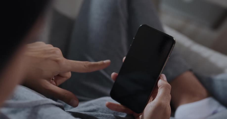 Woman with gray hoodie and pants sits on couch using smartphone