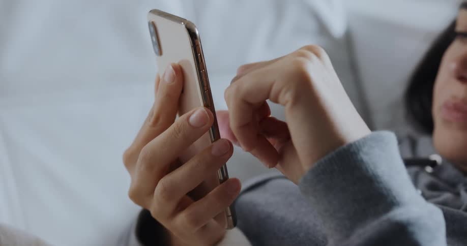 A woman uses her smartphone while lying on a sofa