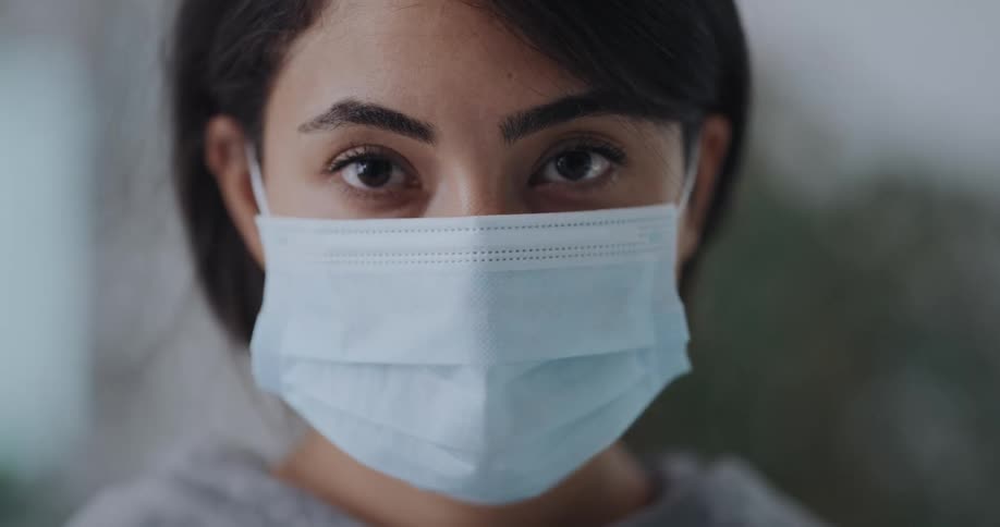 Young woman wearing a blue disposable face mask looking at the camera