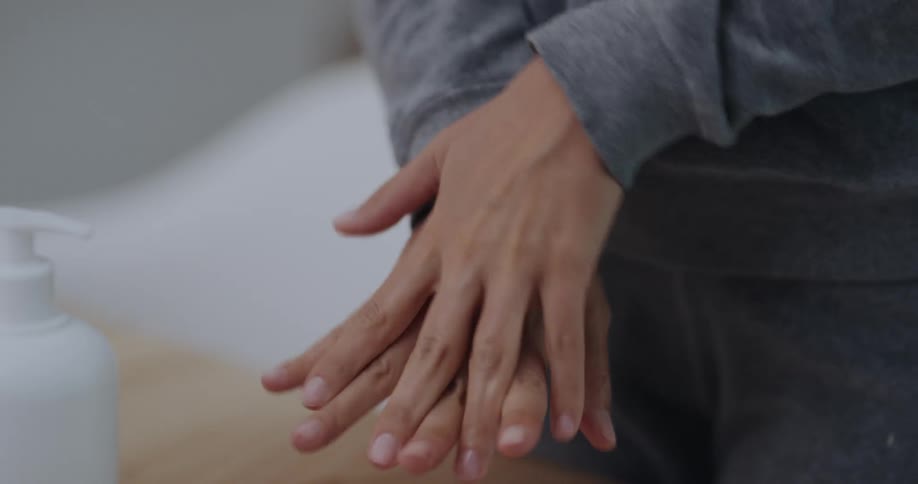 A person rubs hand sanitizer on their hands while standing near a table