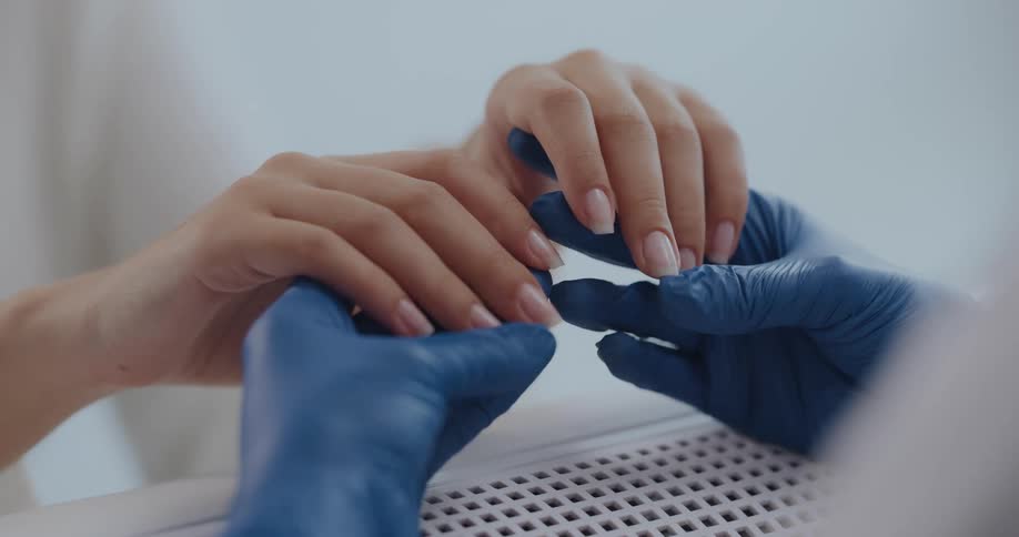 A person wearing rubber gloves is holding another persons hand over an air dryer
