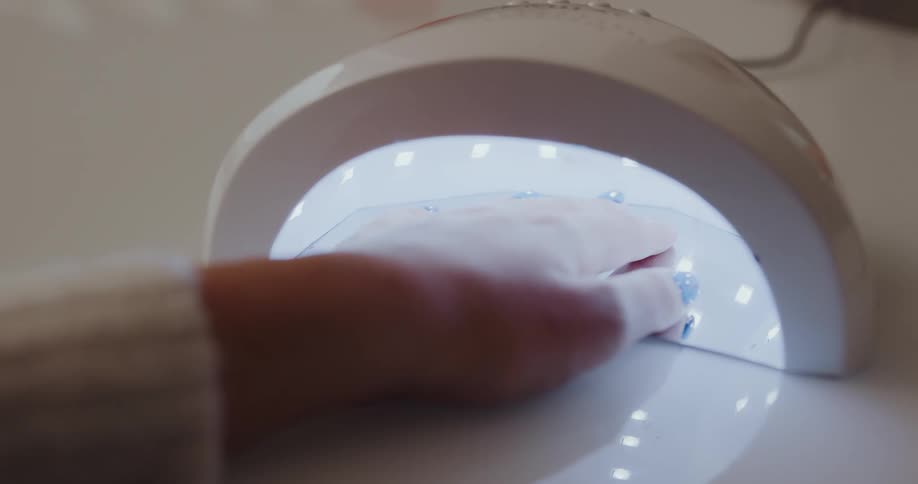 A woman holds her fingers under a uv light to cure nail polish