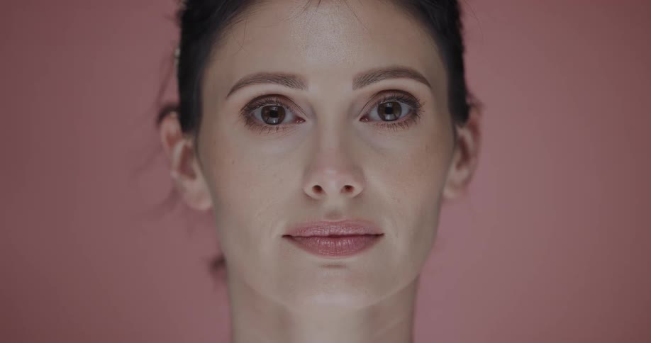 Female model with brown eyes faces the camera with eye contact on pink background