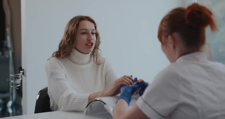 Redheaded manicurist talks with client while examining her hands