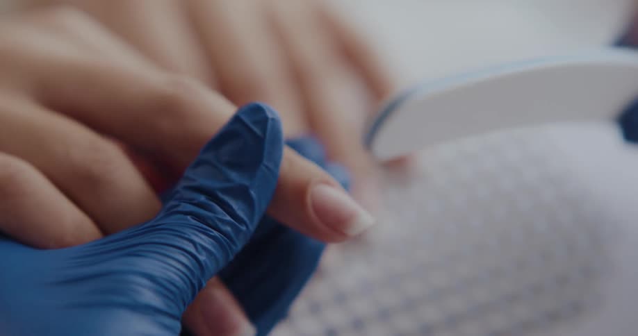 Manicurist wearing blue latex gloves files the nails of a customer
