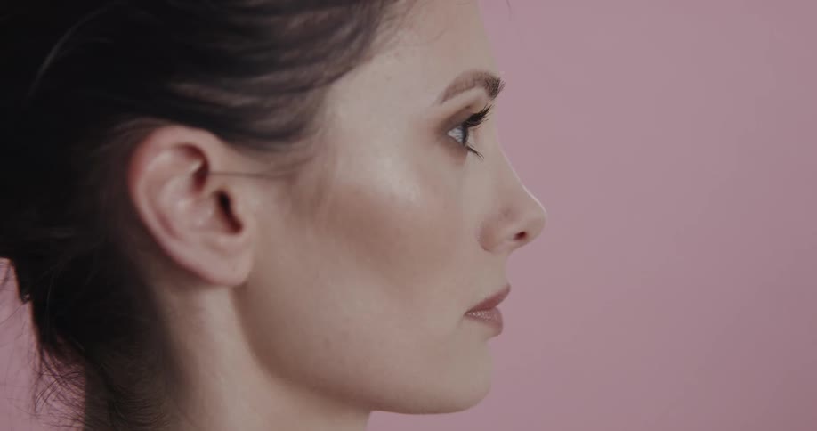 Close up of the face of a woman standing in front of a pink background
