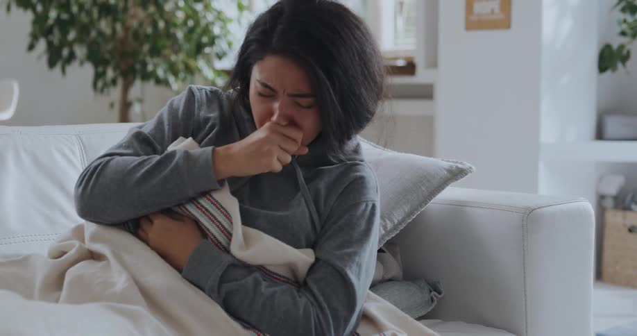 Young sick woman coughs while resting on a couch at home