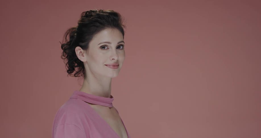 A woman poses in a pink blouse against a pink wall