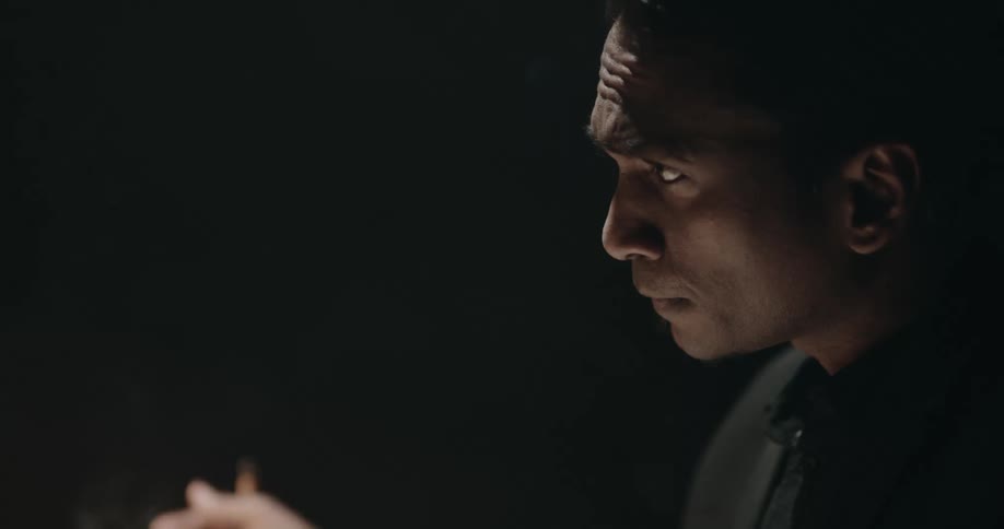 A man is smoking a cigarette in a room at night